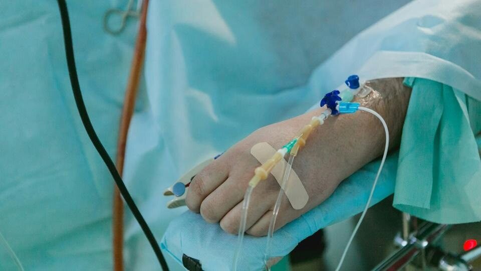 a pale hand curled up on a soft medical cloth with an IV set up attached to the wrist
